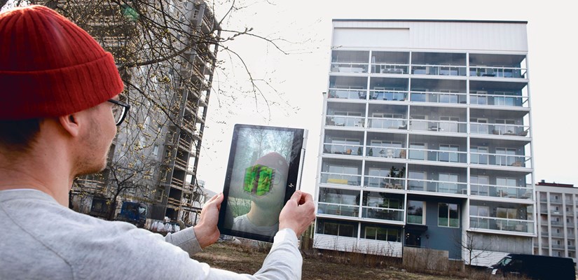 Digitaalinen kaksonen tabletin ruudulla, taustalla kerrostalo