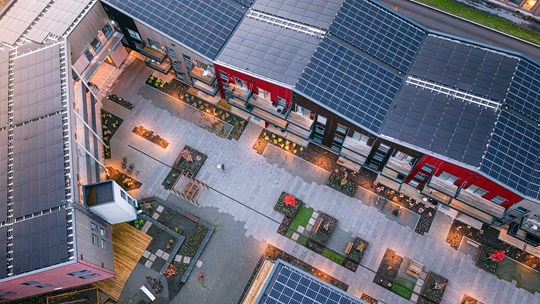 Värikäs pienkerrostalo, joissa katolla aurinkopaneelit ja  pihalla istutuksia.