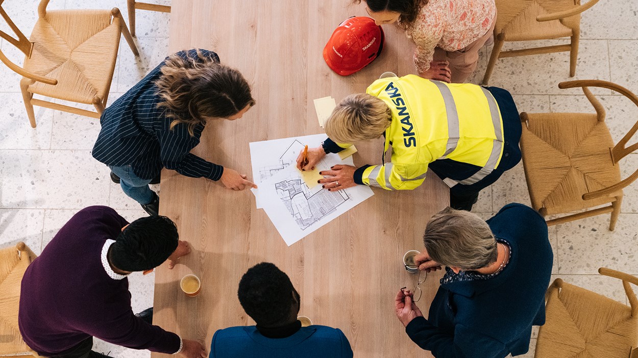 Skanskalaisia pöydän äärellä katselemssa rakennepiirroksia.