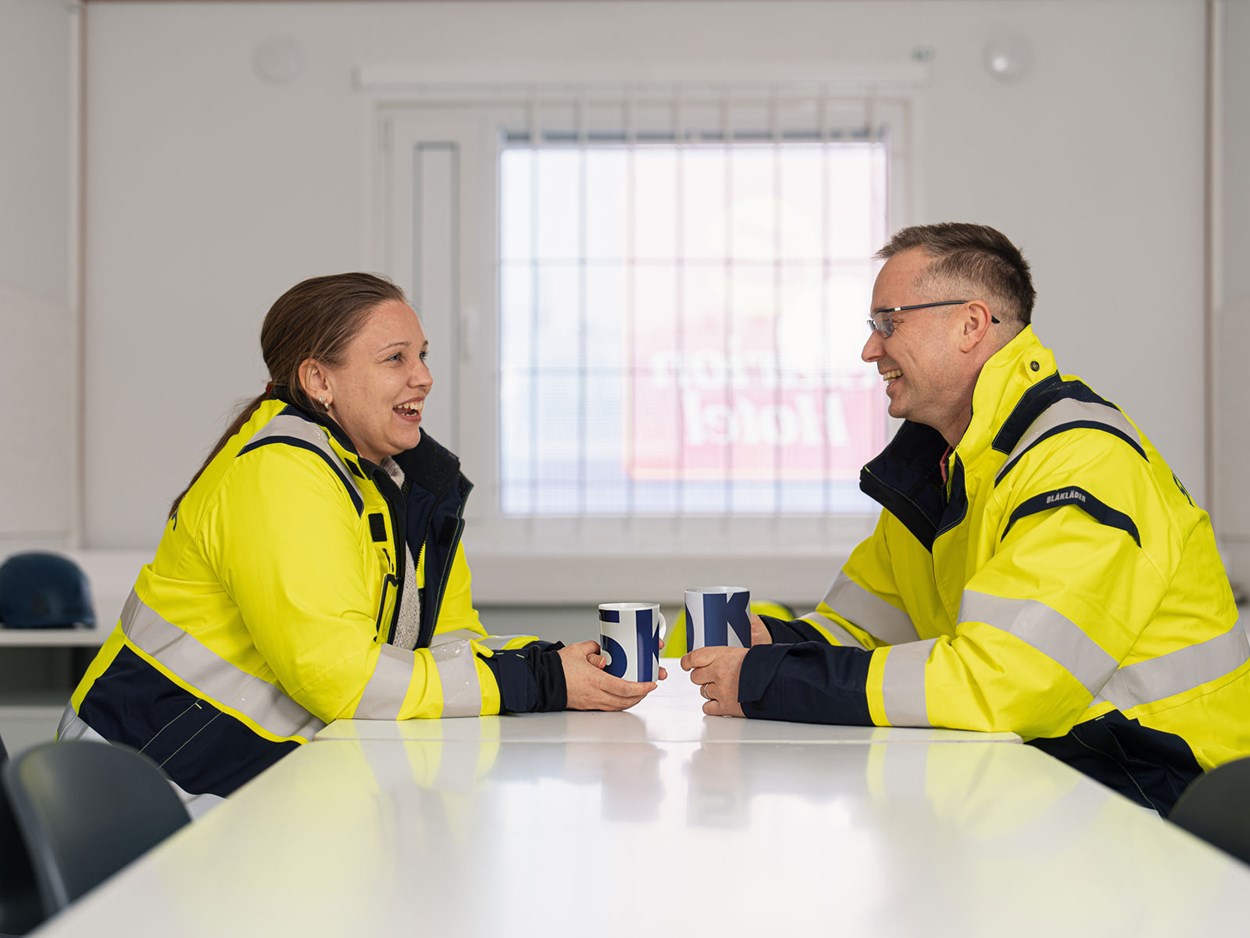 Kaksi skanskalaista kesksutelee kahvitauolla työmaakopissa.