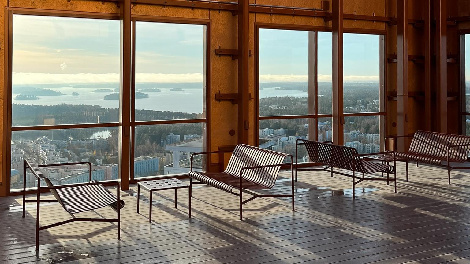 Kuva 33-kerroksen kattoterassilta, jossa on terassiryhmä ja ikkunoita, joista näkyy pitkälle merelle.
