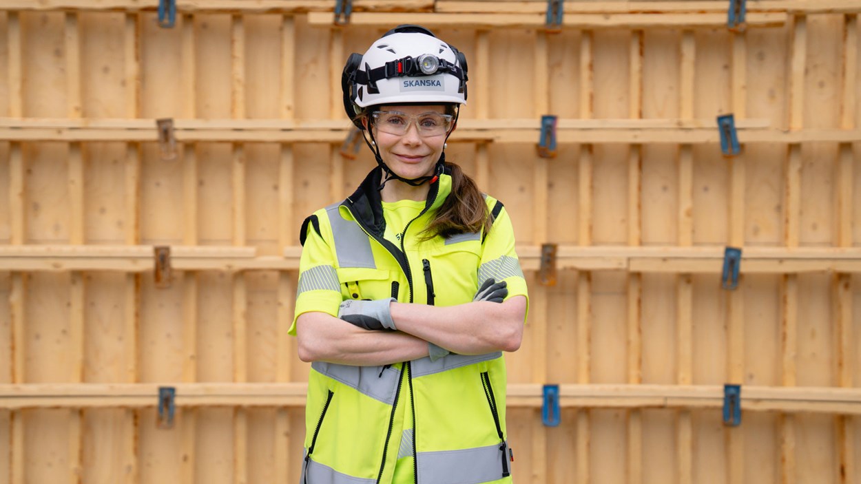 Työnjohtoharjoittelija työmaalla henkilösuojaimet päällä puisen seinän edessä.