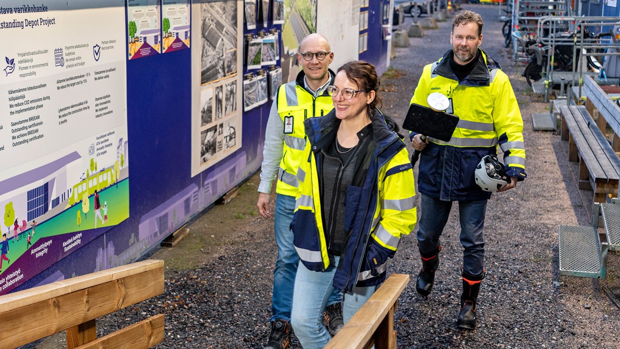 Kolme työmaavarusteista henkilöä kävelee ulkona.