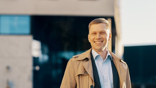 Mikko Lehto hymyilee ulkona rakennuksen edessä 